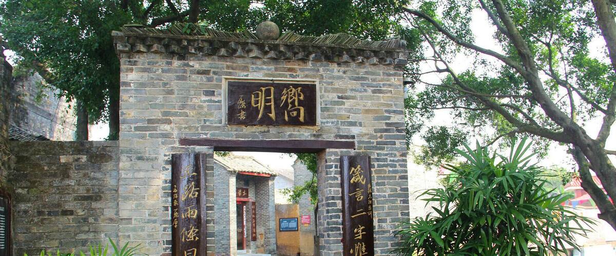 A traditional Chinese gate with inscriptions, leading to a pathway and a building in the background.