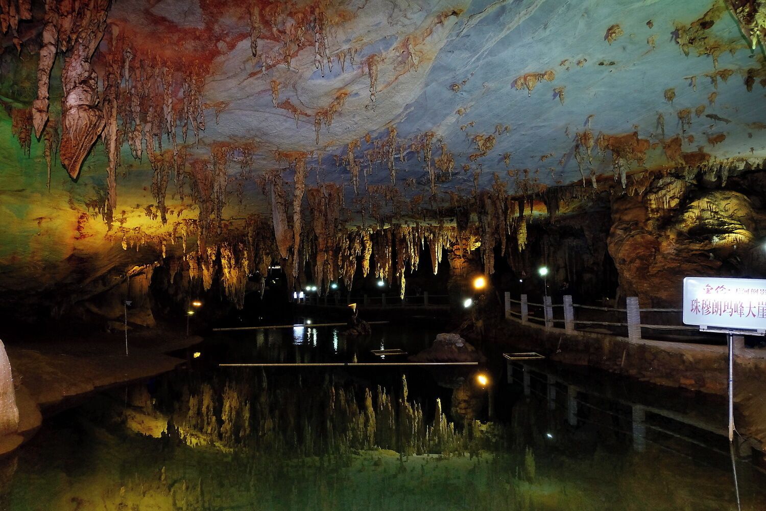 A cave with stalactites and stalagmites, a small pool of water, and a sign in Chinese.