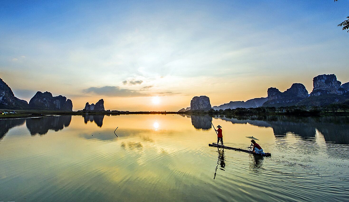 Un lac paisible au coucher du soleil, où deux personnes pagayent dans des canoës, entourés de falaises rocheuses.