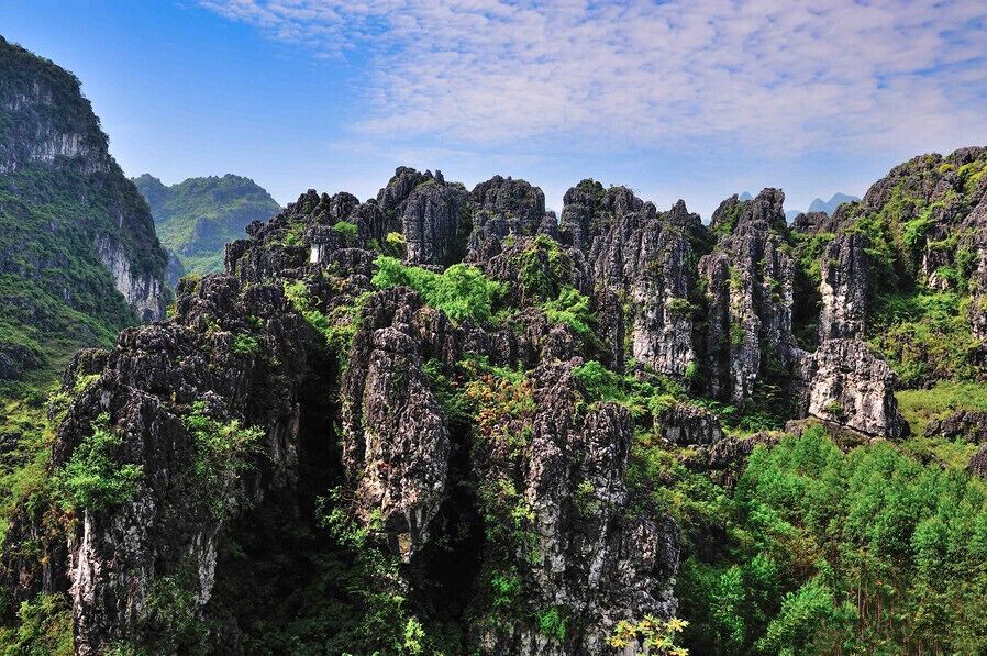 A rugged karst landscape with limestone cliffs and dense green vegetation.