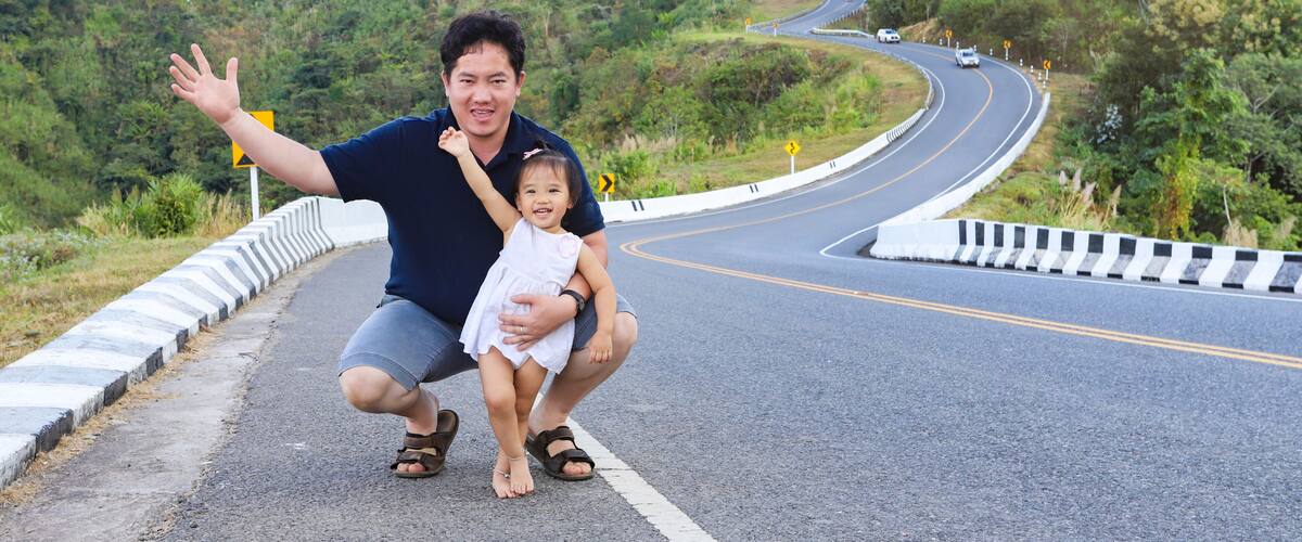 A winding road with a guardrail, surrounded by lush greenery and hills.