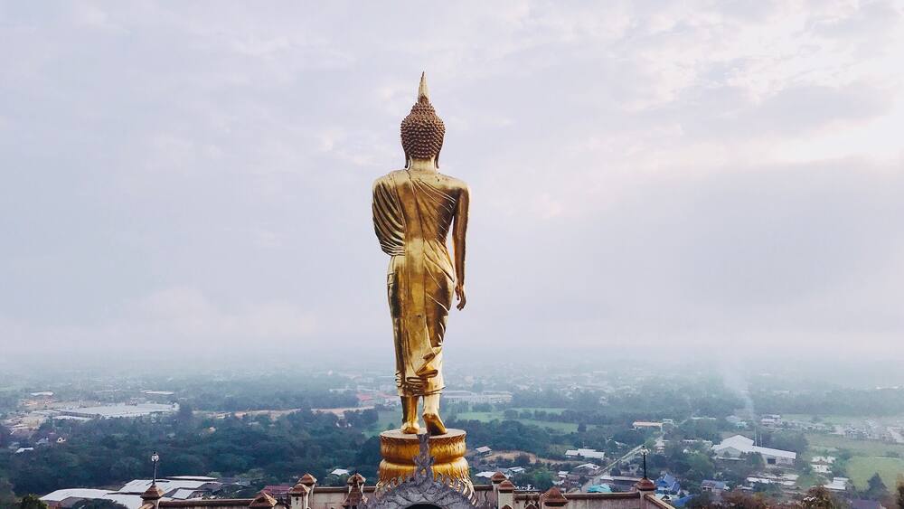 A large golden Buddha statue on a pedestal, surrounded by a stone structure with a view of a cityscape in the background.