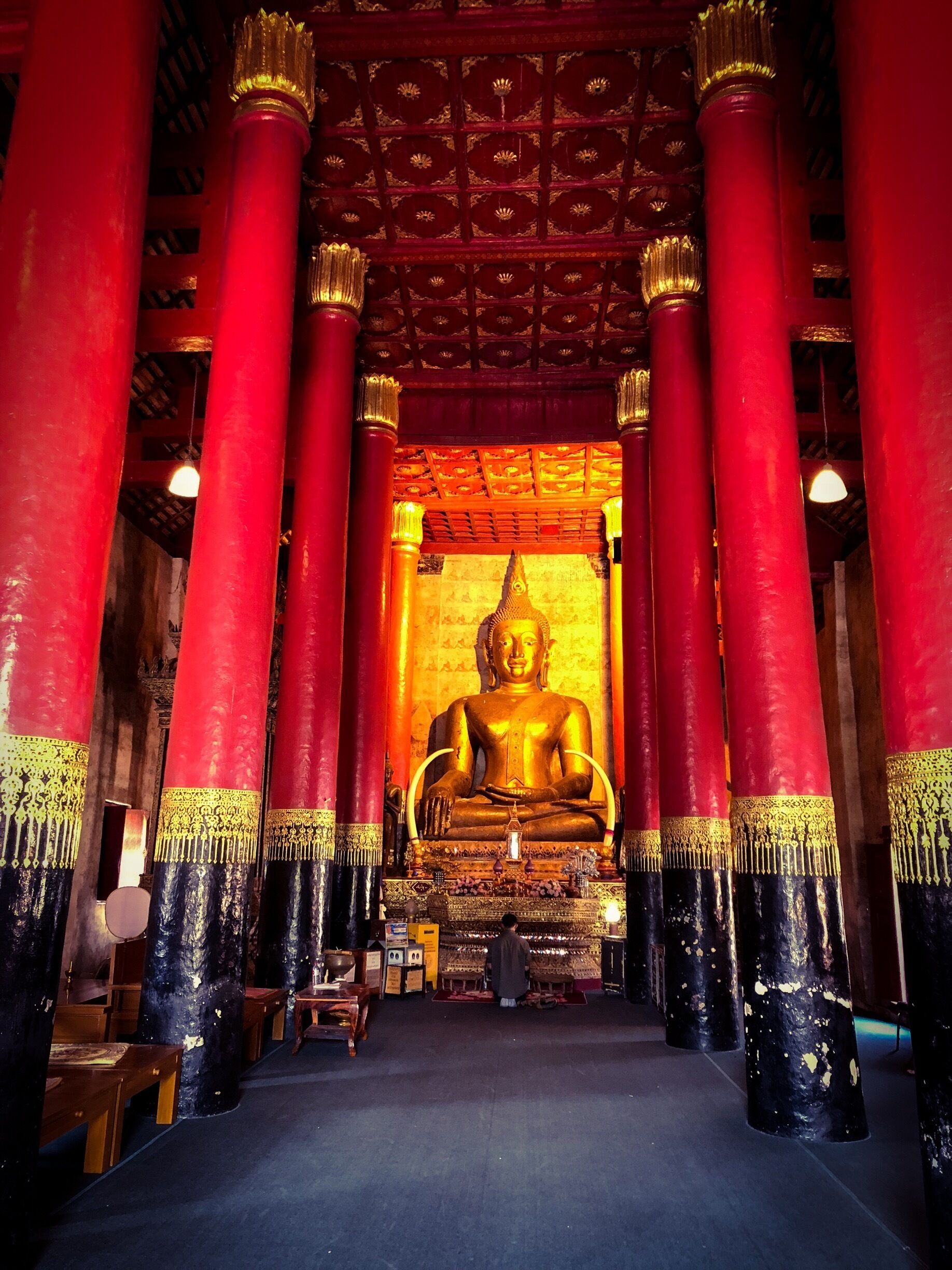 A large golden Buddha statue in a temple with red and black columns.