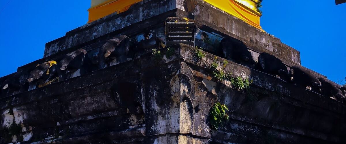 Um stupa dourado com o topo pontudo, diante de um céu azul límpido.