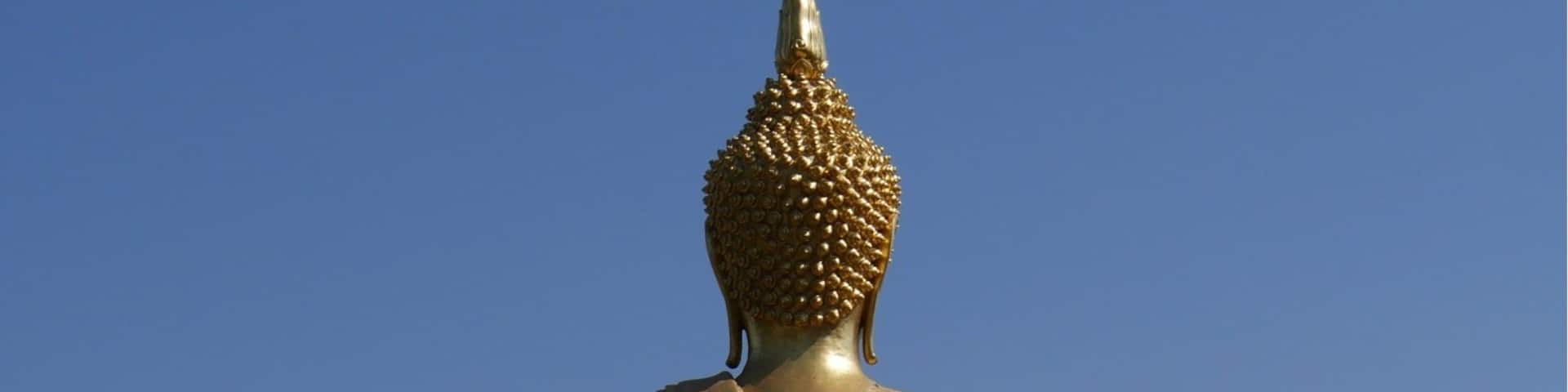 A large golden Buddha statue with a spire, standing on a pedestal with a landscape view in the background.