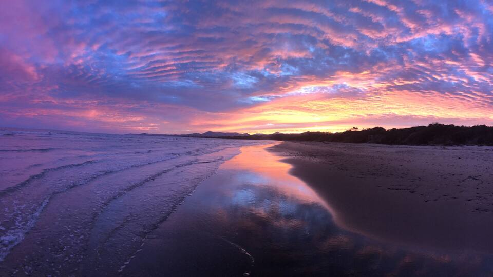 A beach at sunset with a colorful sky and calm water reflecting the sky.