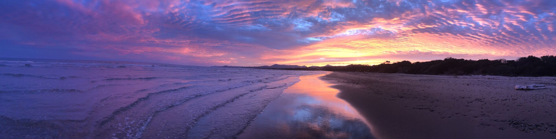 Una playa al atardecer con un cielo colorido y agua tranquila que refleja el cielo.