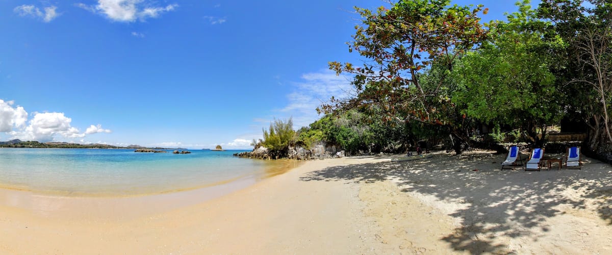 A beach with clear turquoise water, sandy shore, and some trees.