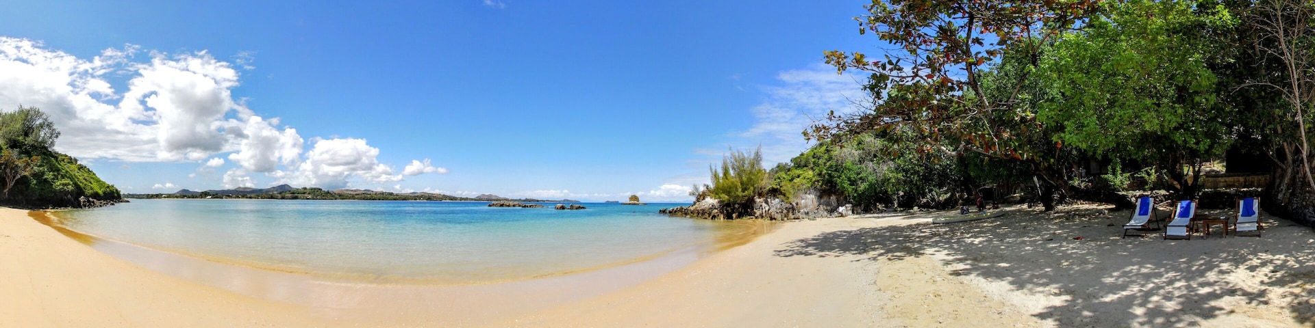 A beach with clear turquoise water, sandy shore, and some trees.