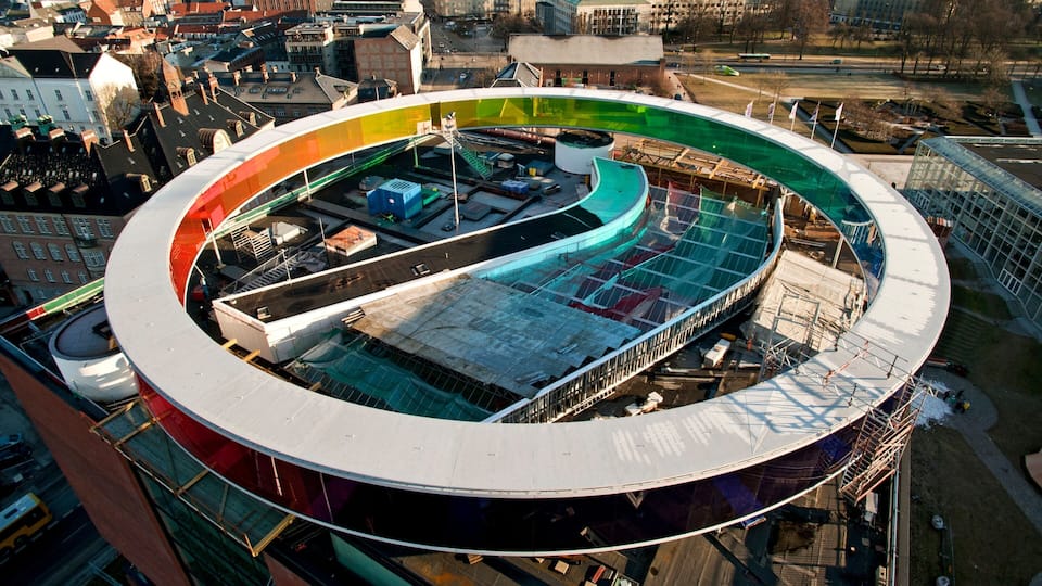 A large, circular stadium with a multi-colored roof, surrounded by urban buildings.
