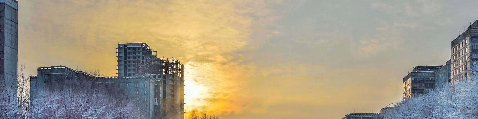 Winter golden sunset and mist rises above the water
of little river. Frosty weather, trees and grass on the banks are covered with fluffy hoarfrost - urban winter landscape with buildings and bridge