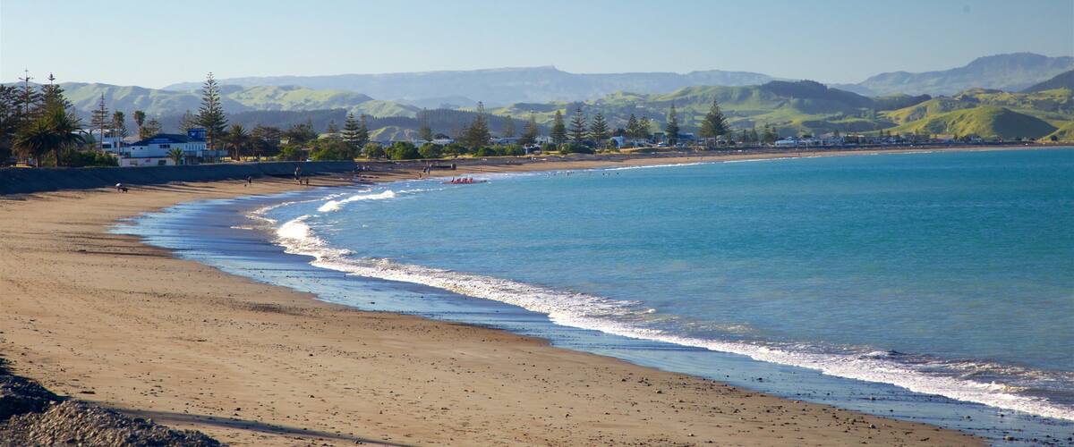 A sandy beach with gentle waves, a clear blue sky, and distant mountains.