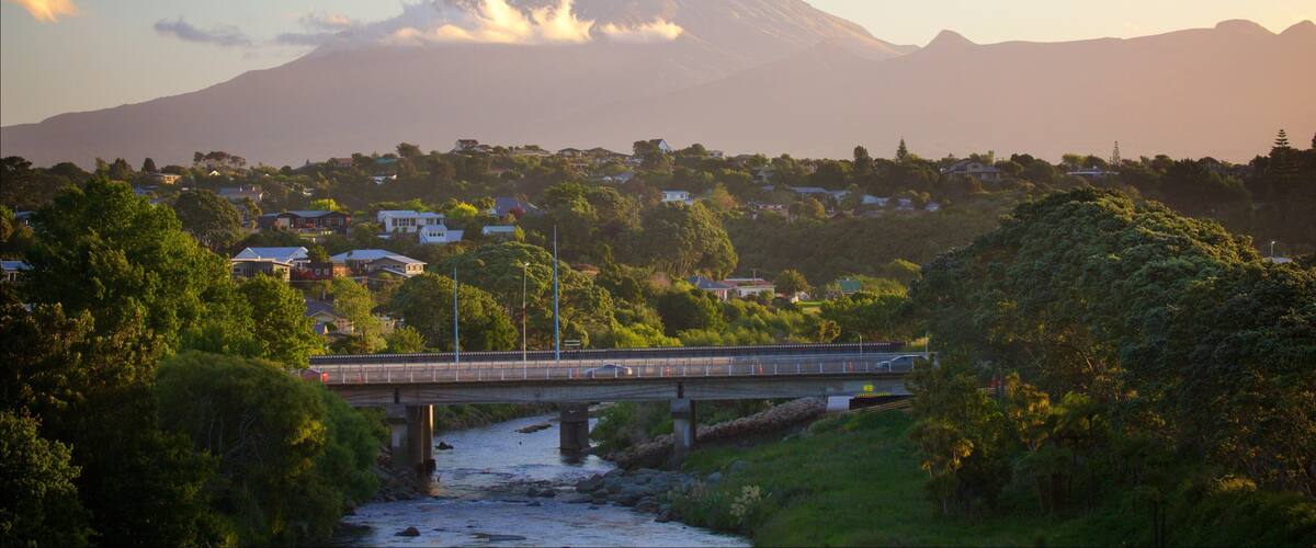 A bridge over a river, a town with houses, and a snow-capped mountain in the background.