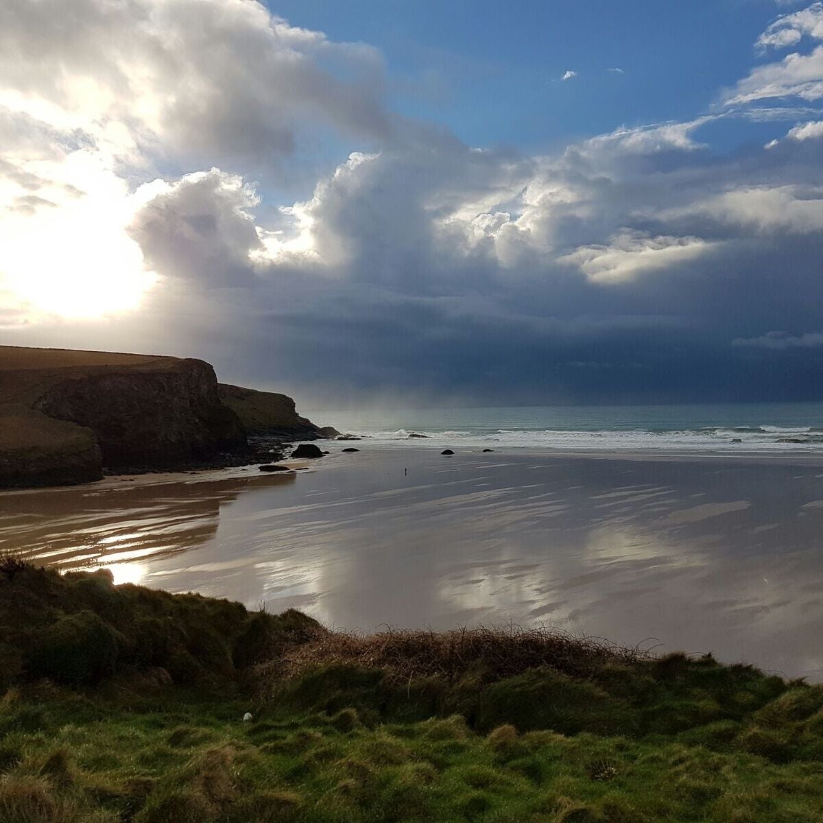 A coastal landscape with cliffs, a beach, and a cloudy sky.