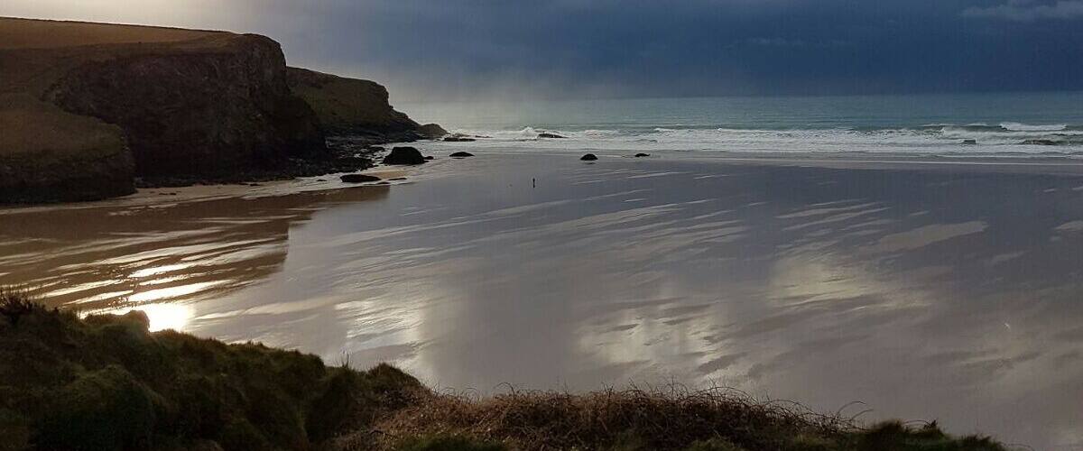 A coastal landscape with cliffs, a beach, and a cloudy sky.