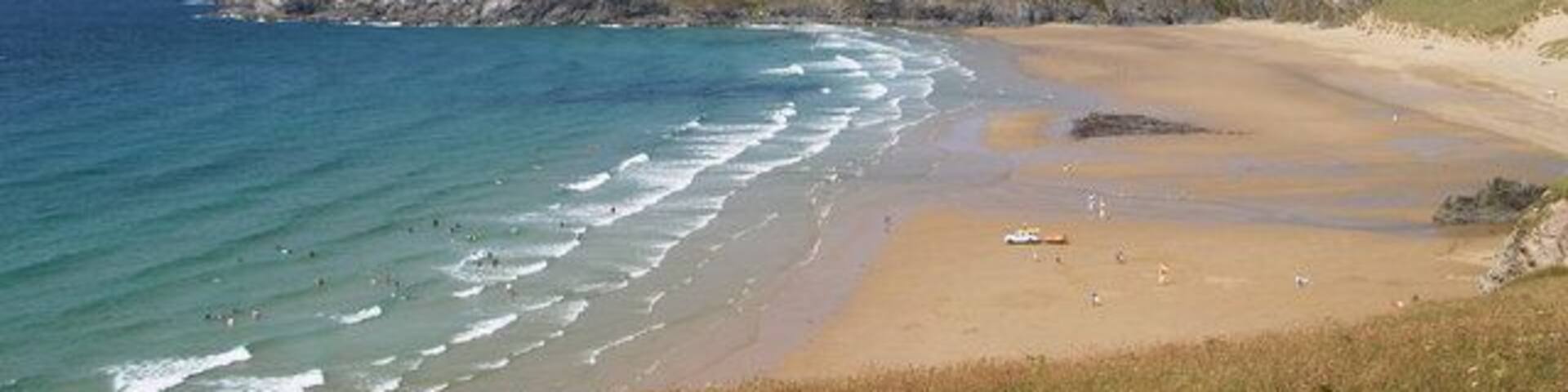 A coastal landscape with a sandy beach, rocky cliffs, and the ocean.
