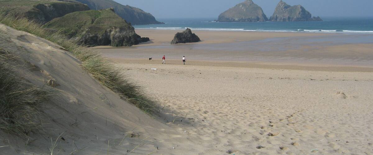 A sandy beach with rocky outcrops and grassy hills in the background.
