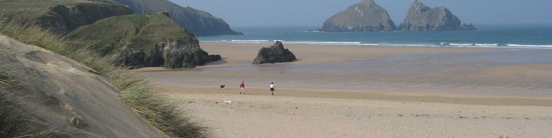 A sandy beach with rocky outcrops and grassy hills in the background.