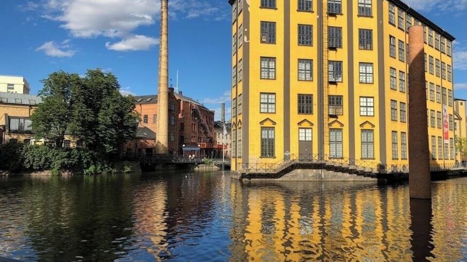 Un edificio amarillo con una chimenea alta, un río y un árbol.
