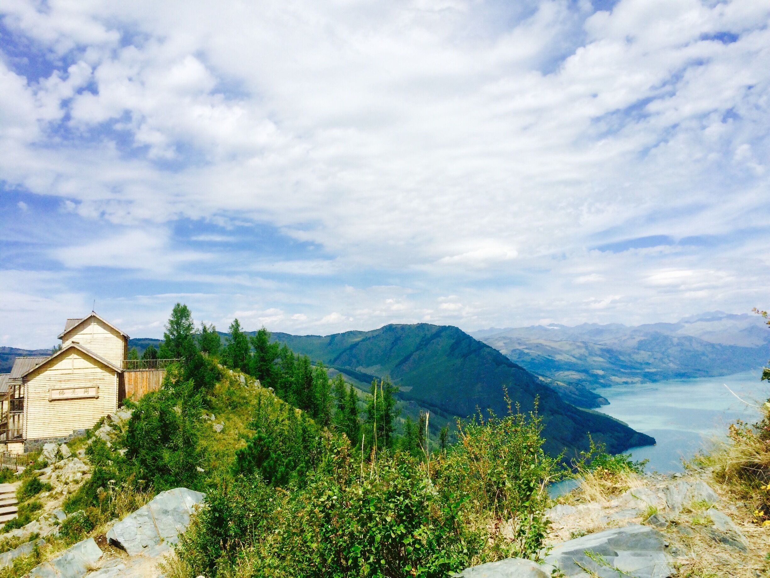 A wooden cabin on a hillside overlooking a lake and mountains.