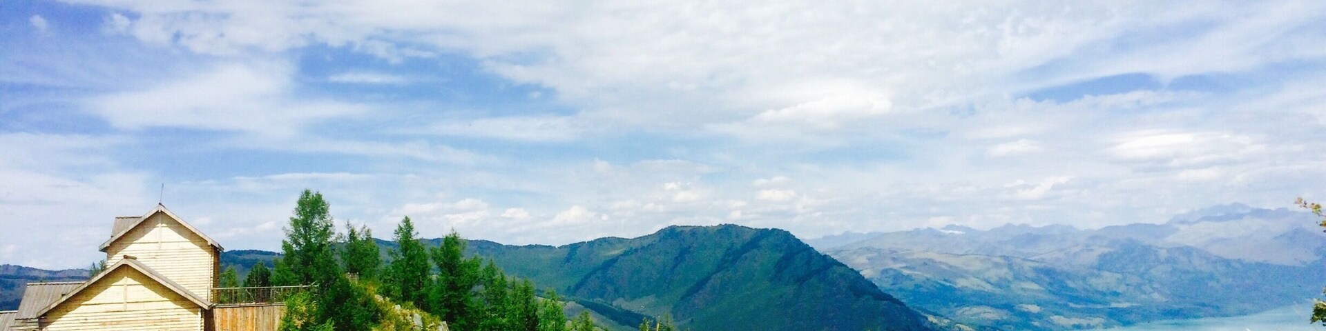 A wooden cabin on a hillside overlooking a lake and mountains.