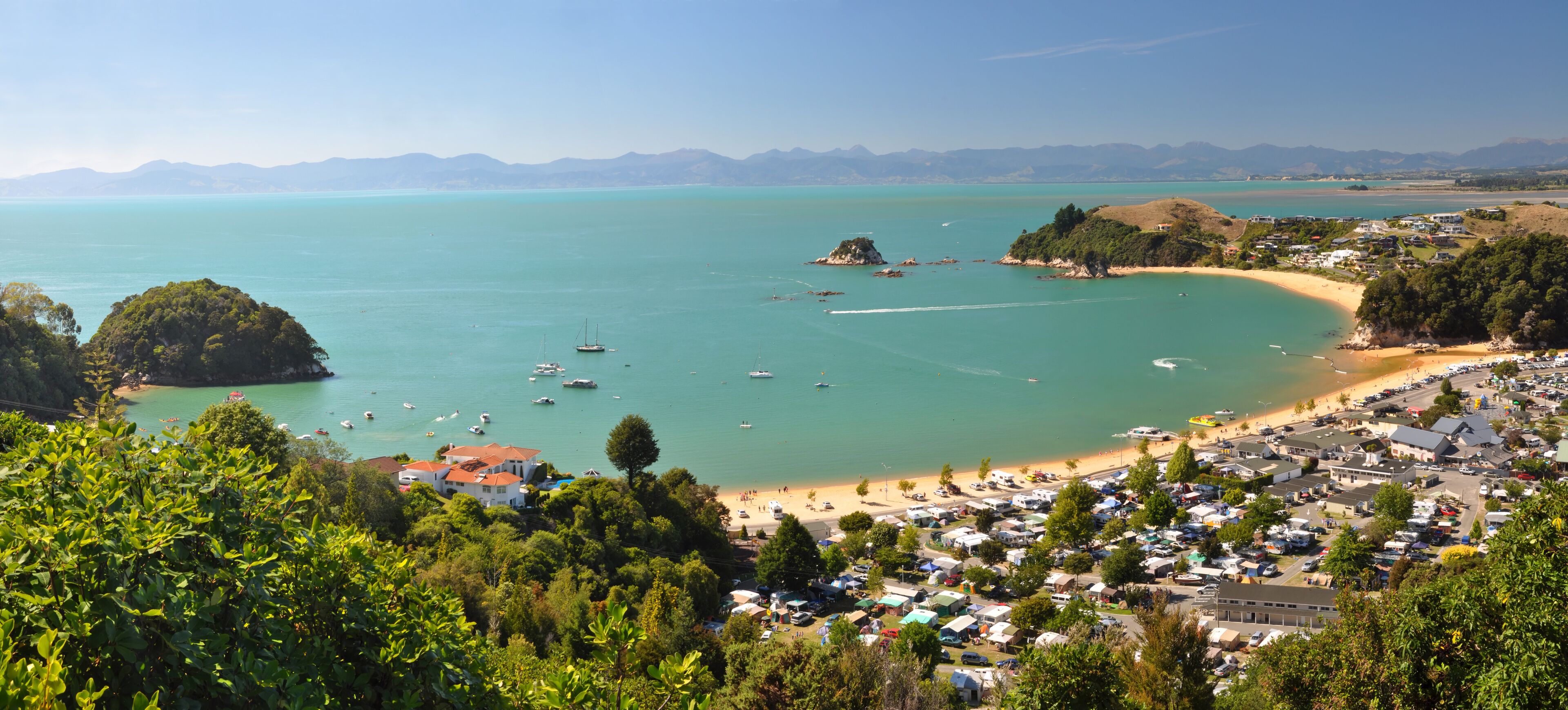 A coastal town with a beach, boats, and a mountainous backdrop.