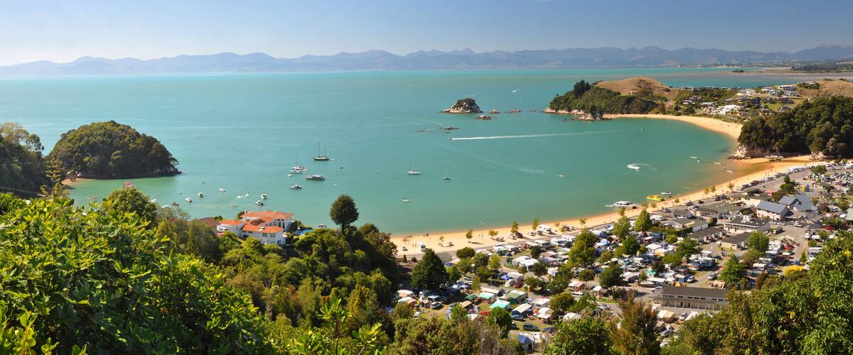 A coastal town with a beach, boats, and a mountainous backdrop.