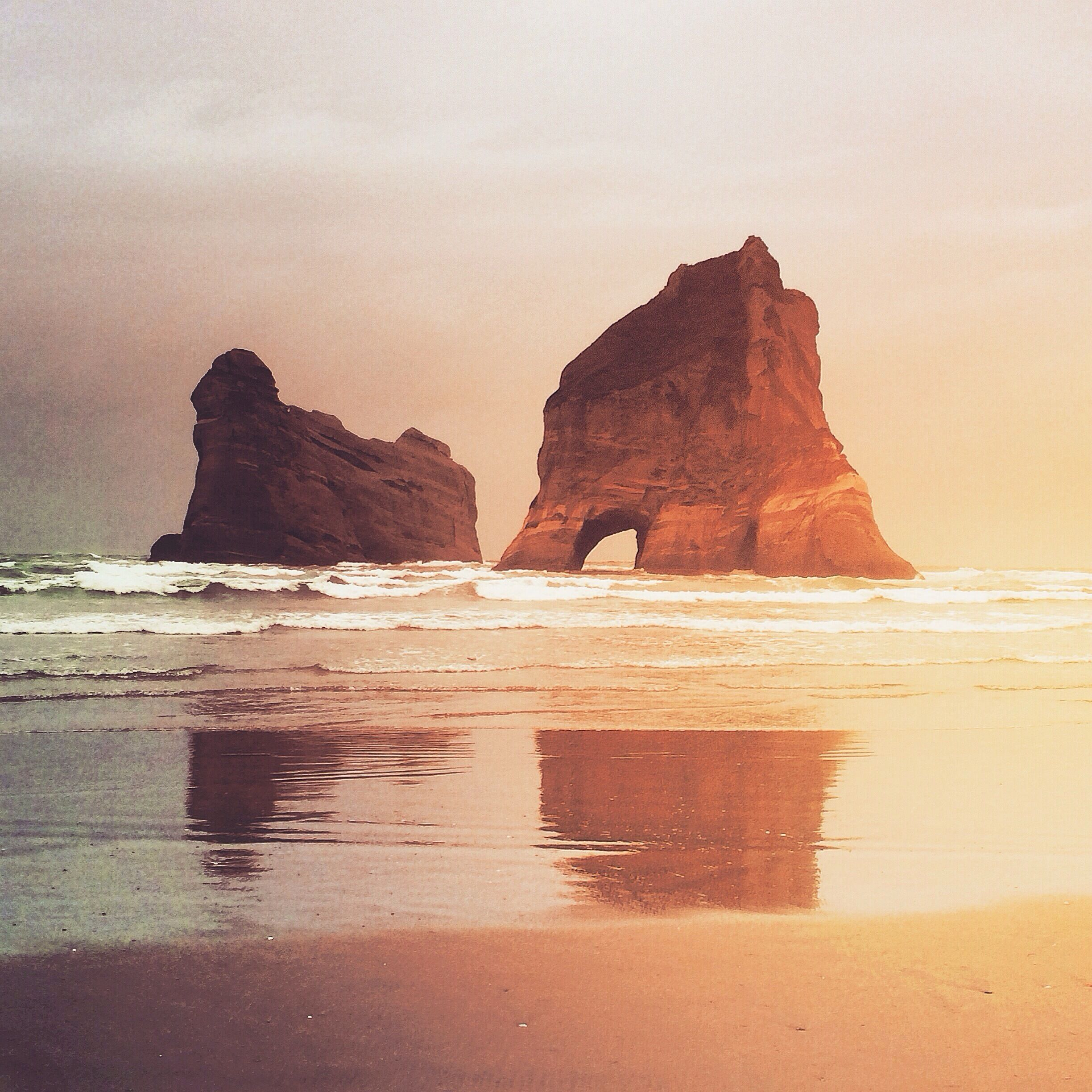 A beach with two large rock formations and waves crashing onto the shore.