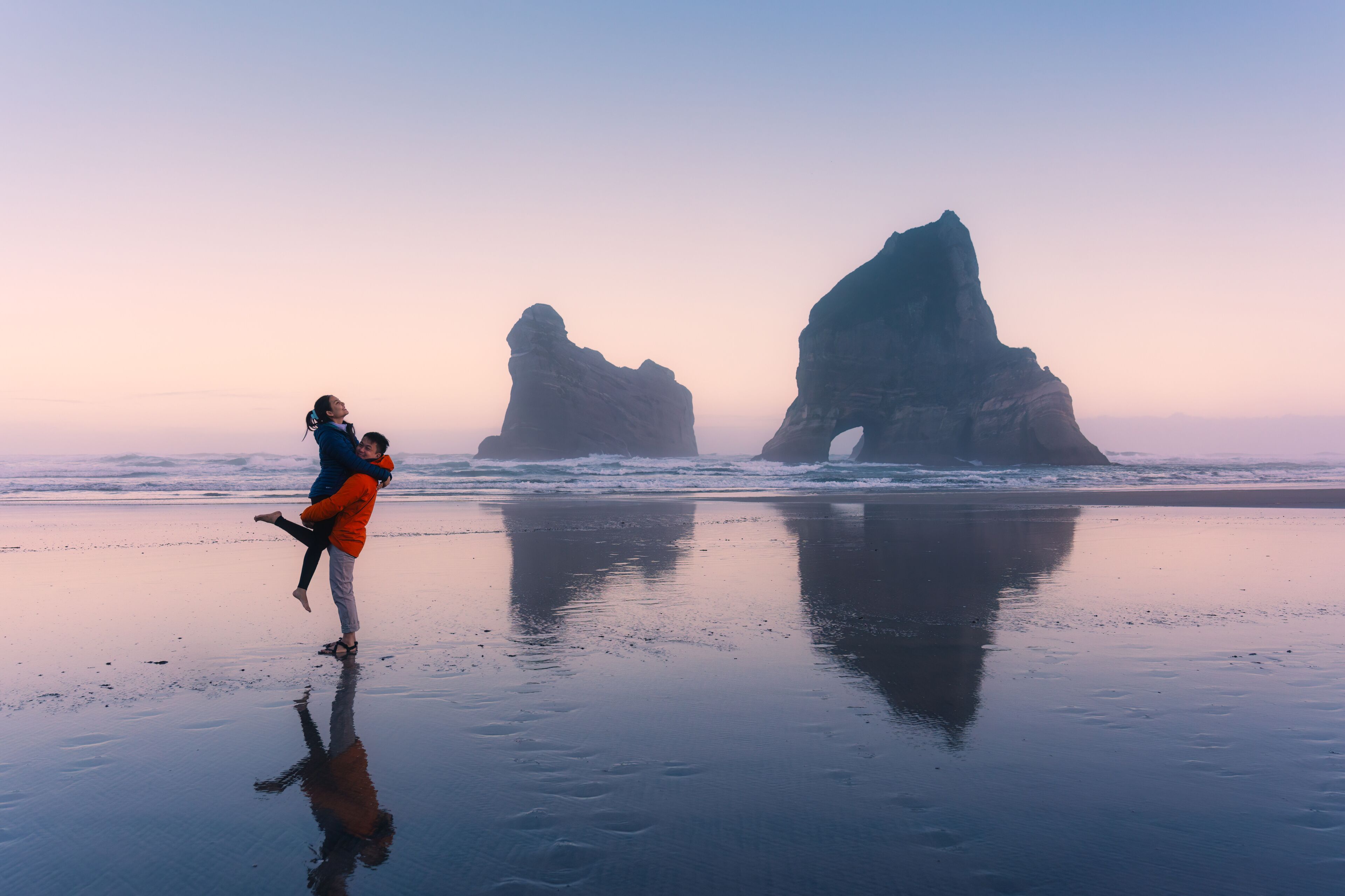 Asian couple enjoying on Wharariki beach with iconic archway island at New Zealand