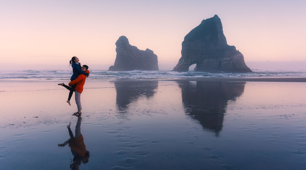 Asian couple enjoying on Wharariki beach with iconic archway island at New Zealand