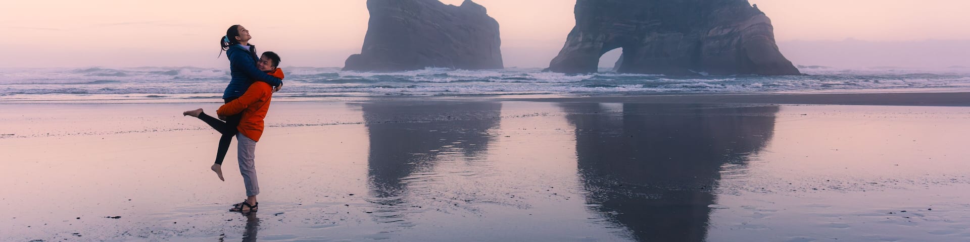 Asian couple enjoying on Wharariki beach with iconic archway island at New Zealand