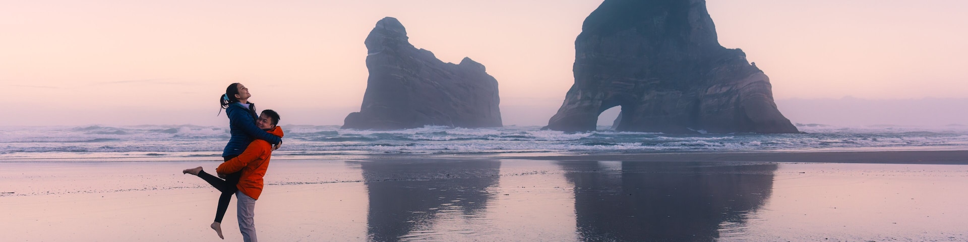 Asian couple enjoying on Wharariki beach with iconic archway island at New Zealand
