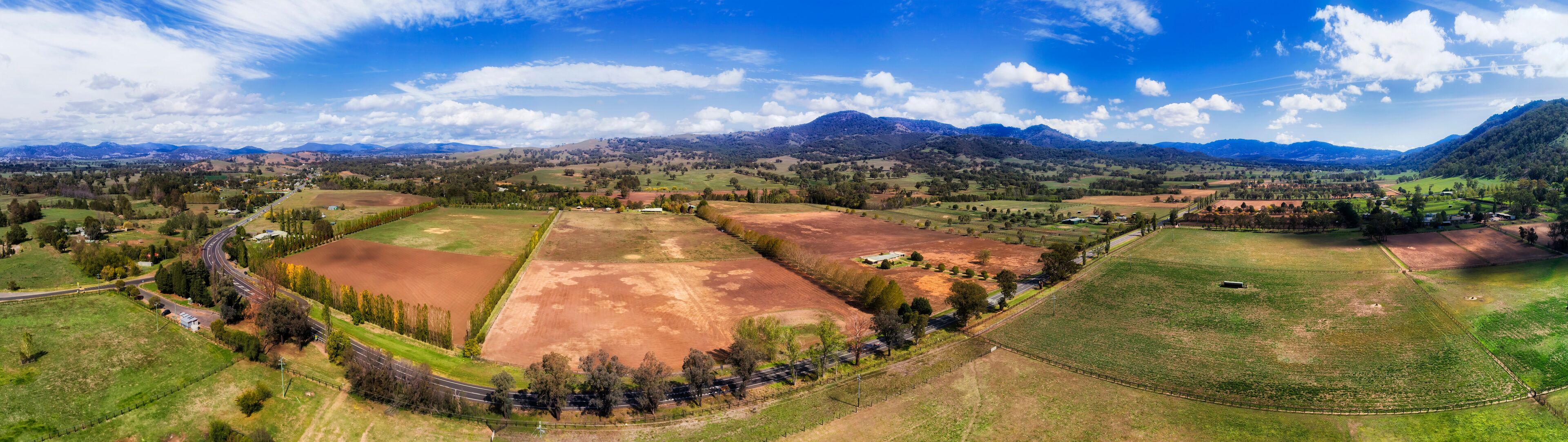 A panoramic view of a rural landscape with fields, roads, and distant mountains.