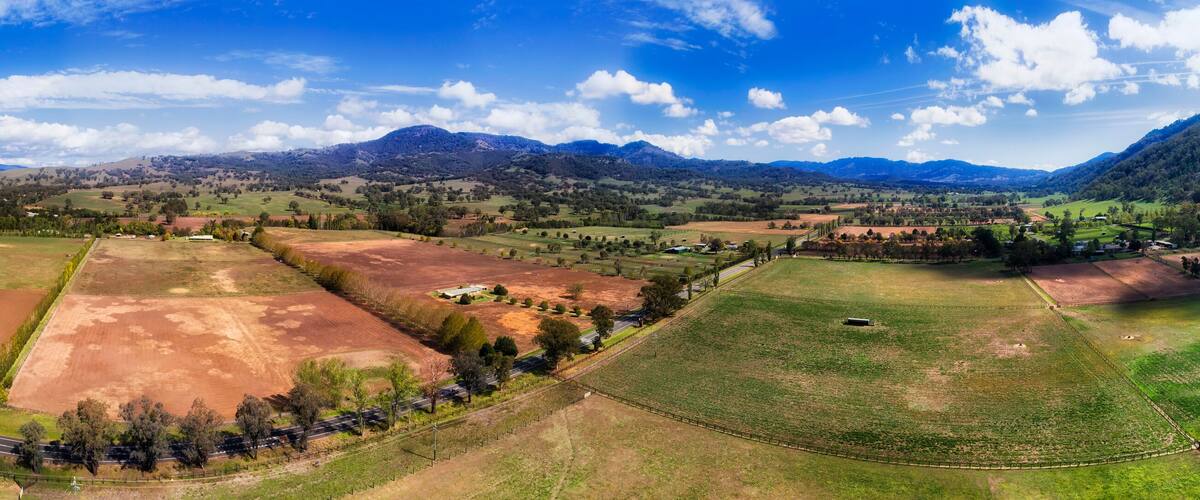 A panoramic view of a rural landscape with fields, roads, and distant mountains.