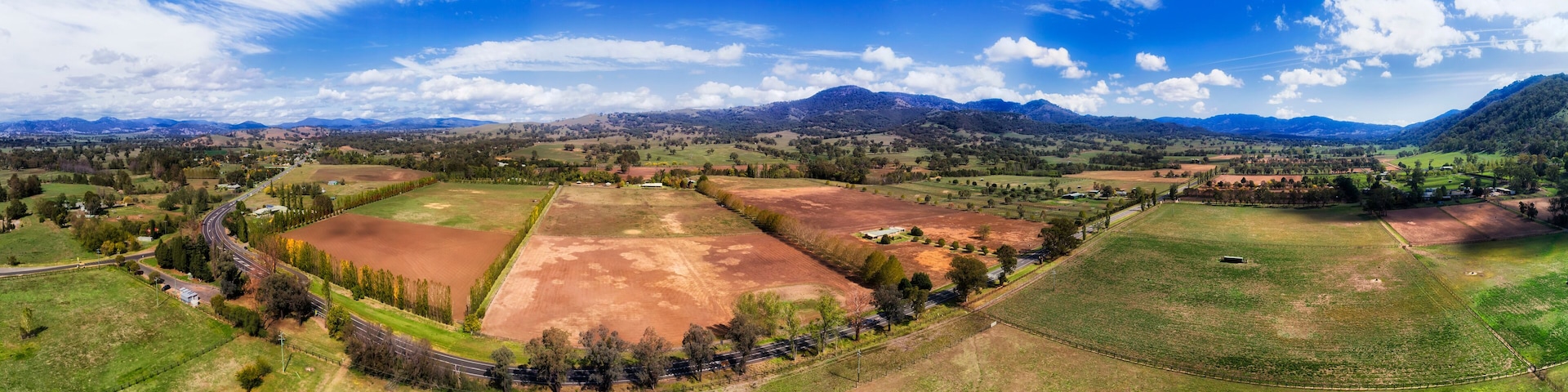 A panoramic view of a rural landscape with fields, roads, and distant mountains.