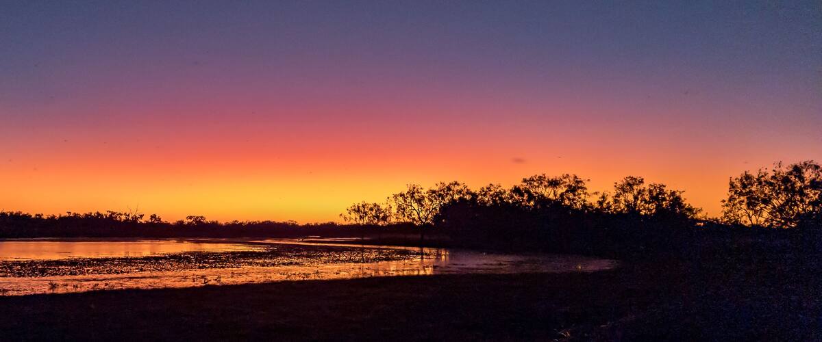 A sunset over a river with trees silhouetted against the sky.