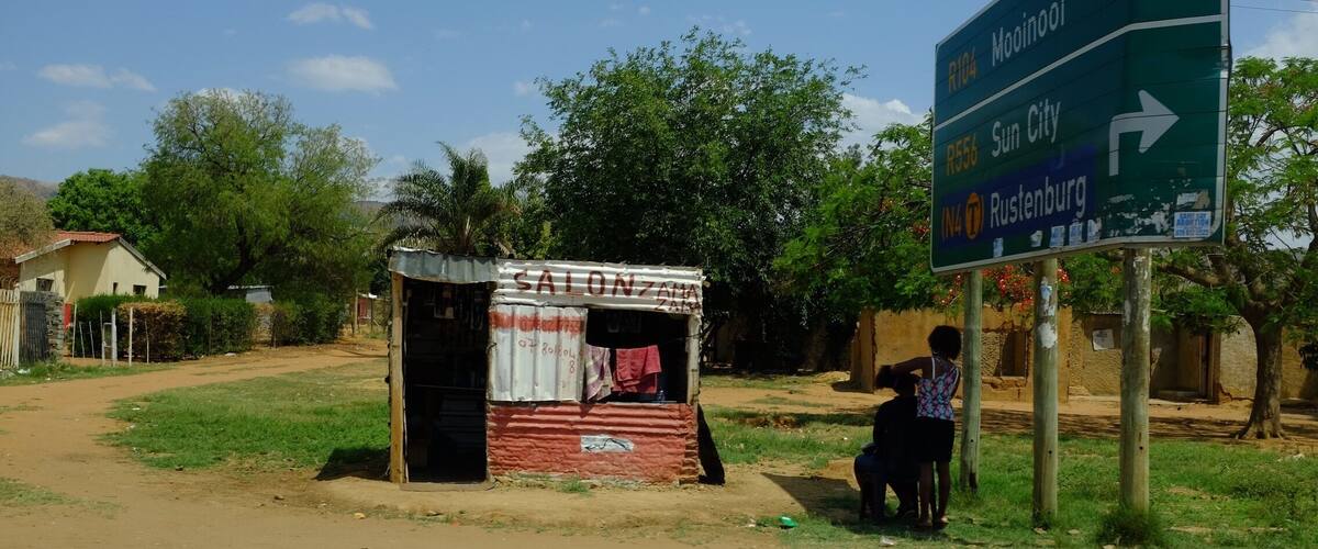 A roadside sign with directions to Mooinoci, Sun City, and Rustenburg, and a small roadside stall with a sign reading "SALON ZAMA".