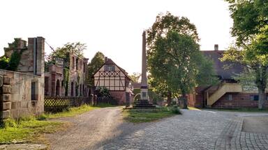A cobblestone street flanked by historic buildings, including a half-timbered house and a tall monument.