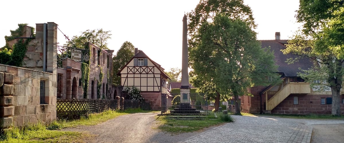 A cobblestone street flanked by historic buildings, including a half-timbered house and a tall monument.