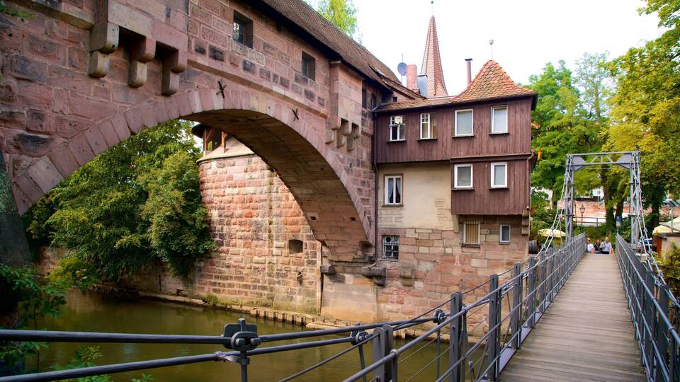A stone bridge over a river, with a wooden walkway and a historic building in the background.