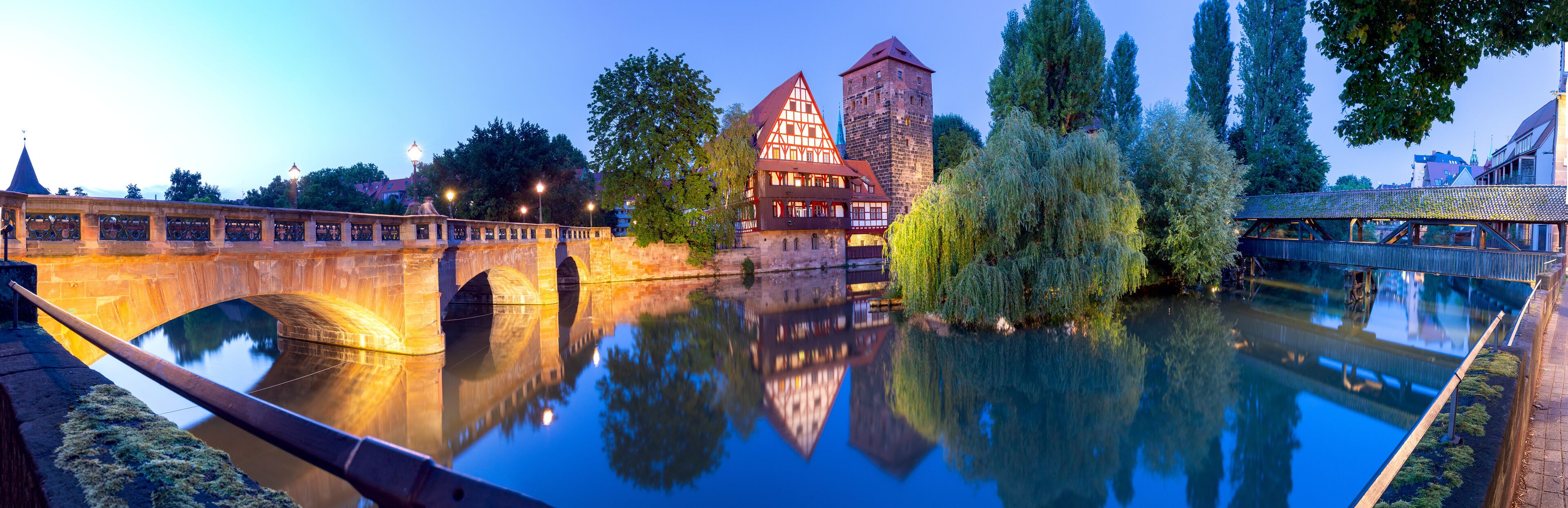 Un puente histórico, un castillo y un río que refleja las estructuras.