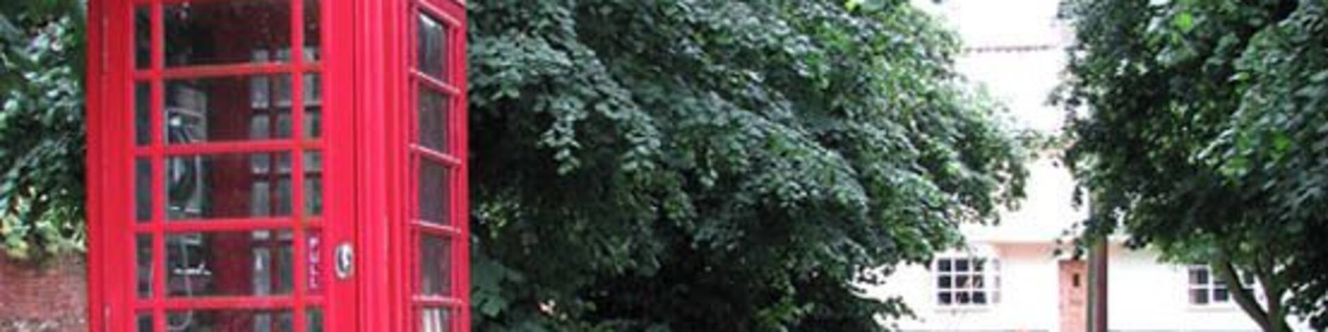 K6 Telephone box on green by Boosey's Lane. New Buckenham is a village located on the Norfolk-Suffolk border. Interestingly, its street plan is still based on the old medieval grid pattern. 16th century houses, built from wattle and clay on timber frames, stand side by side with flint and brick cottages, often hidden behind Georgian and later brick facades > 1394567. The 18th century market cross, situated in the village centre, serves as a shelter > 40538. The village has two pubs, the George > 1394575 and the Kings Head, a number of local shops and a general store which is combined with a bakery and a post office > 1394579. There is a large common designated a Conservation Area to the east of the village. The remains of a castle are on the edge of the village, and near it there is the first place of worship, the now restored St Mary's Chapel, which was replaced by St Martin's church > 1394594.