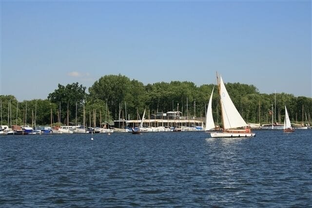 A marina with sailboats, a docked ferry, and a forested shoreline.