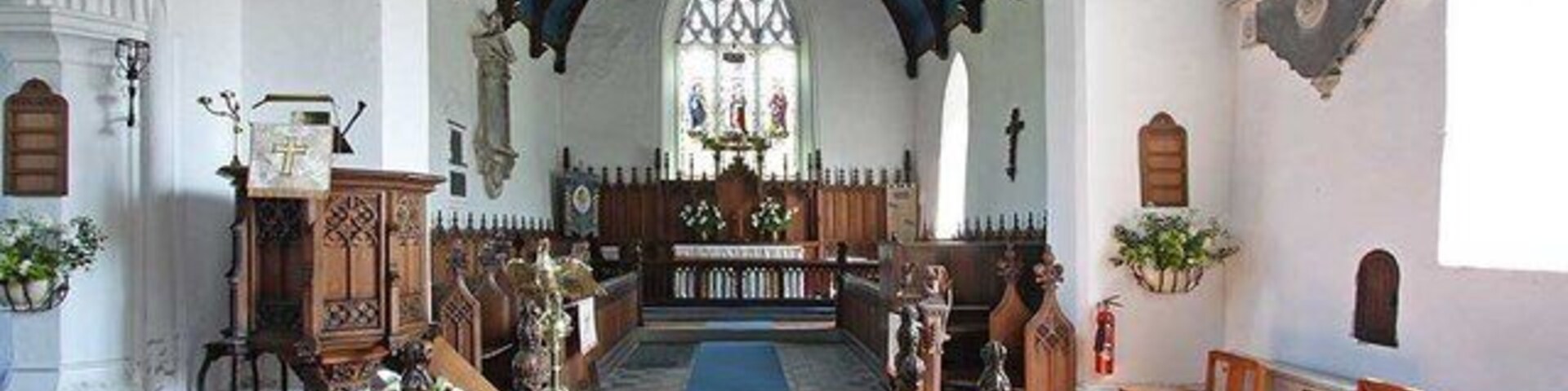 Interior de iglesia con bancos de madera, alfombra azul y un techo alto abovedado.