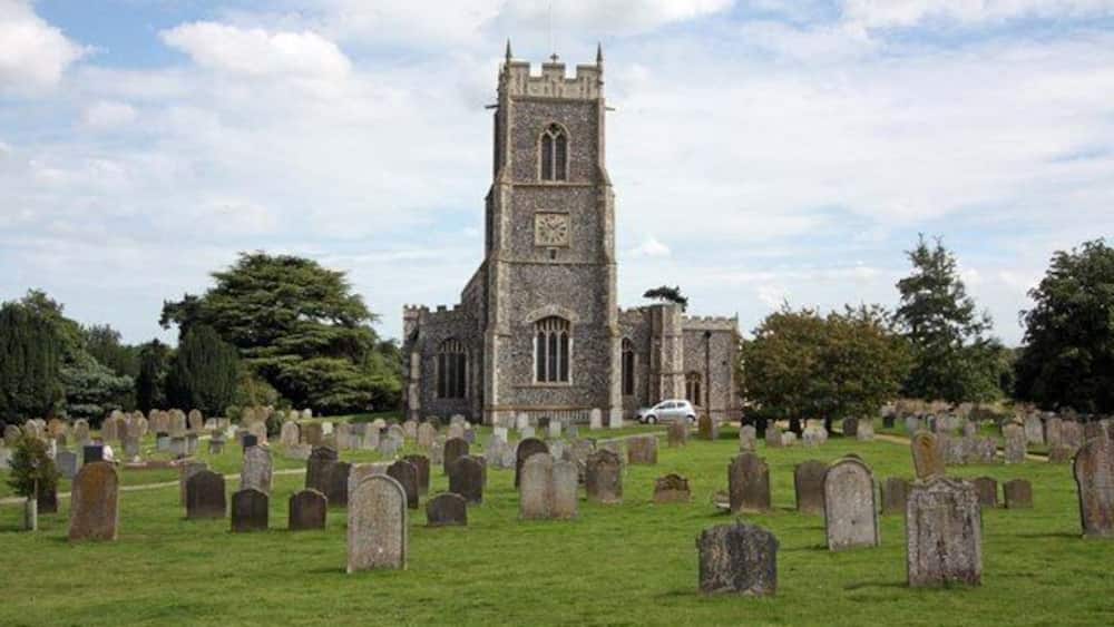Eine Kirche mit einem hohen Turm und ein Friedhof mit vielen Grabsteinen.