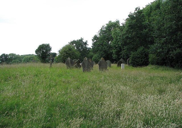 A cemetery with headstones in a grassy field, surrounded by trees.