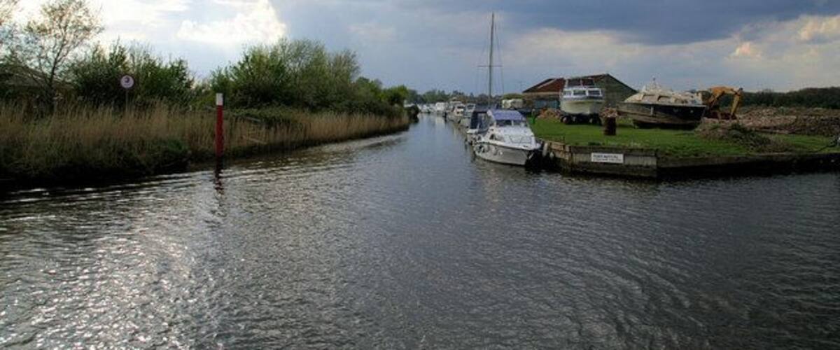 A narrow canal with boats, a construction site, and a cloudy sky.