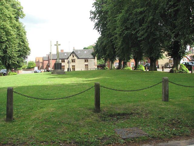 A grassy area with a chain-link fence, a church, and large trees.