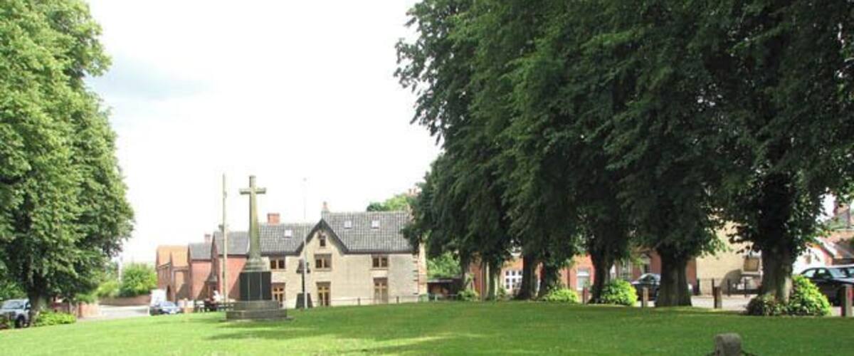 A grassy area with a chain-link fence, a church, and large trees.