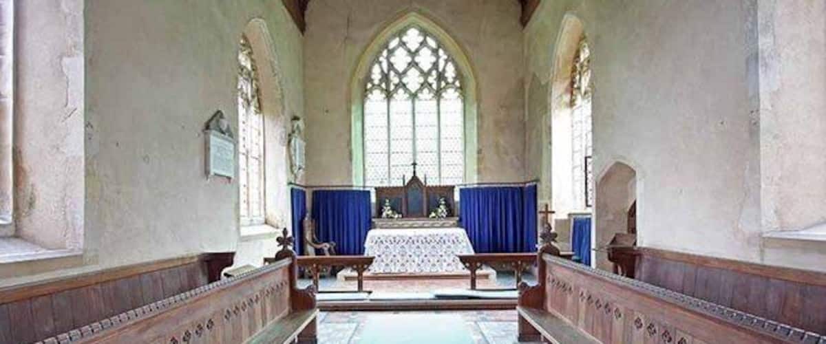 A church interior with arched windows, wooden pews, and a central altar.